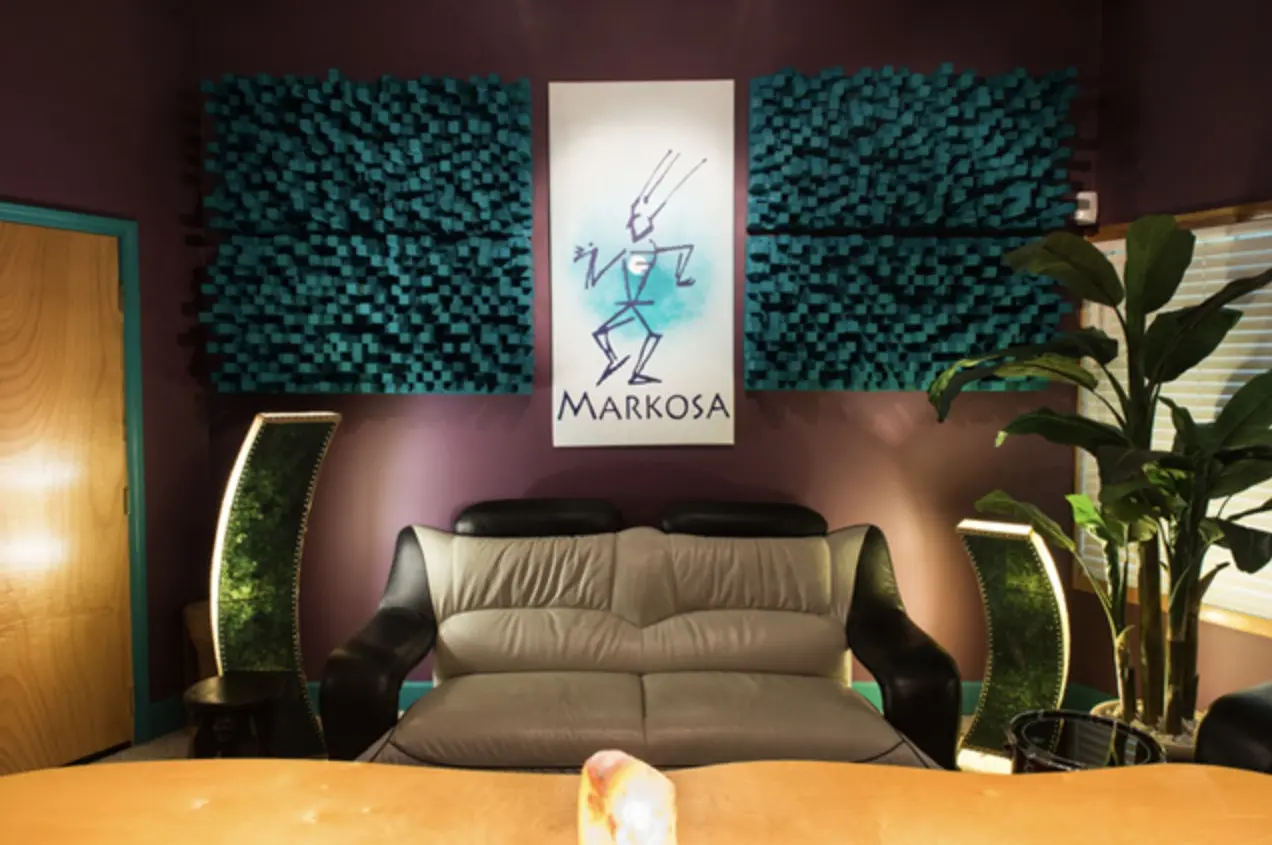 Control room seating under the Markosa banner, with teal acoustic panels and plants